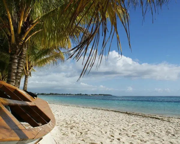 Mauritius pora deszczowa. Drewniana łódź na piaszczystej plaży pod palmami, turkusowe morze i błękitne niebo z chmurami.