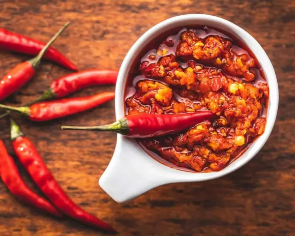 Scharfes Essen stillen: Eine Schale mit feuriger Chilisauce und frischen roten Chilis auf einem Holztisch.