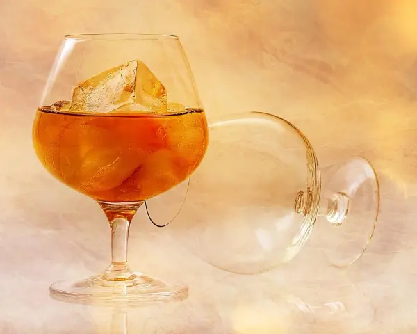 Kieliszek z bursztynowym płynem i lodem, obok pusty, przewrócony kieliszek. Idealny sposób, jak pić brandy.