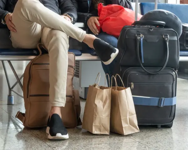 Osoby czekają na lotnisku z bagażem. Widać plecak, torby podróżne i papierowe torby na zakupy. To typowy nouvelair bagaż.