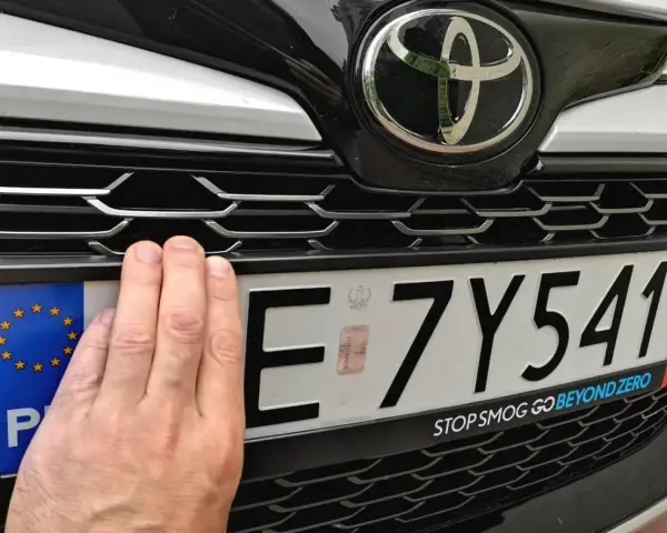 Dłoń zasłania część tablicy rejestracyjnej E 7Y541. Pod nią widoczny jest napis "STOP SMOG GO BEYOND ZERO".