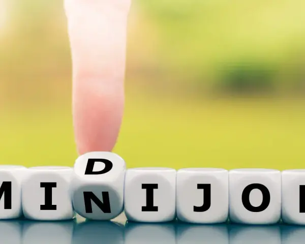 Würfel zeigen "MINIJOB". Ein Finger dreht den Würfel mit "D" zu "N", um "MINIJOB" zu bilden. Ideal für flexible Stunden pro Woche.