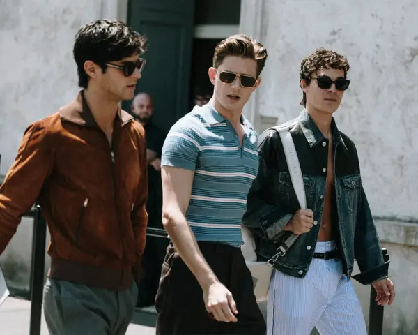 Tre uomini camminano insieme, uno con giacca marrone, uno con polo a righe e uno con giacca di jeans. Un look uomo di stile.