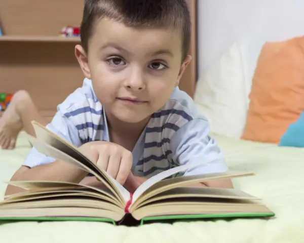 Chłopiec leży na łóżku z otwartą książką. To świetny sposób, jak zachęcić dziecko do czytania.
