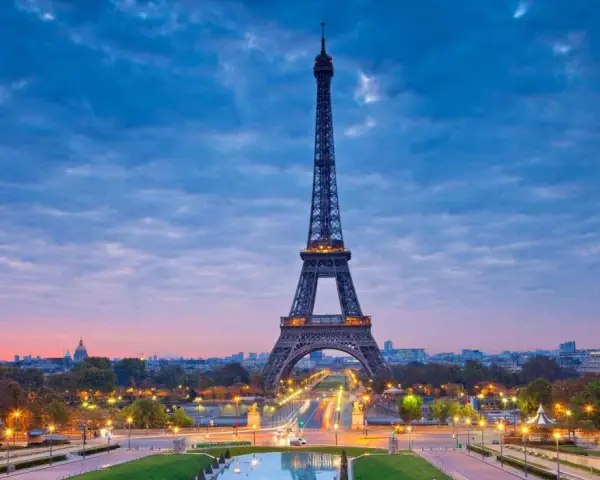 Torre Eiffel iluminada al atardecer, uno de los iconos franceses más reconocidos, con el cielo azul y nubes rosadas.