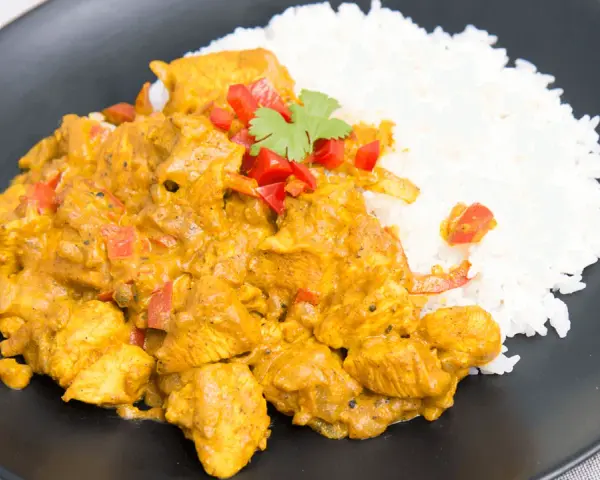 Pyszny kurczak curry fit z ryżem, papryką i kolendrą na czarnym talerzu. Idealny posiłek dla dbających o linię.