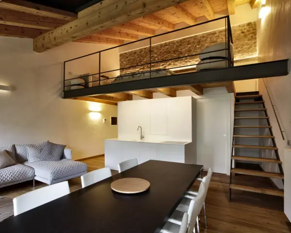 Modern living space with a loft bedroom accessible by stairs. The **soppalco soffitto basso** features a metal railing and a stone wall.