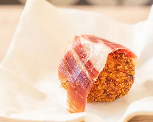 Croqueta dorada con jamón ibérico, servida sobre papel blanco.