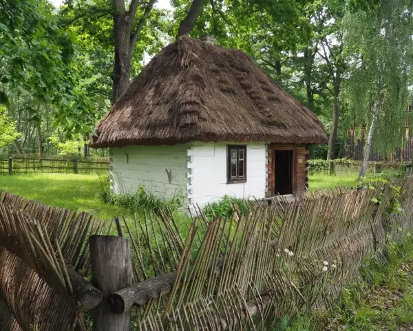 Drewniana chata z krytym strzechą dachem i płotem z gałęzi. Wspaniałe radom atrakcje, które przenoszą w przeszłość.