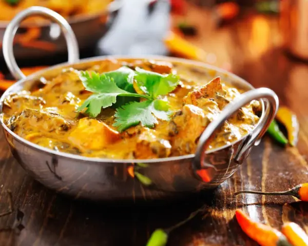 Ein cremiges Curry, garniert mit Koriander, umgeben von bunten Chilis. Ein Genuss für Liebhaber indischer Gerichte.