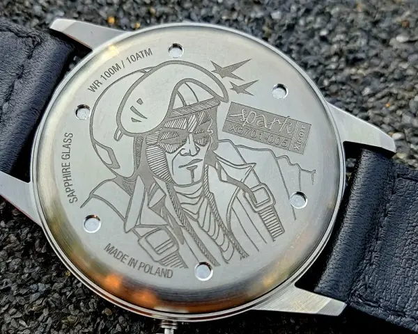 Napis na deklu zegarka: "MADE IN POLAND", WR 100M/10ATM, SAPPHIRE GLASS. Grawer przedstawia pilota w hełmie i goglach.