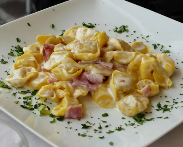 Tortellini panna e prosciutto, un piatto cremoso e saporito, guarnito con prezzemolo fresco su un piatto bianco.