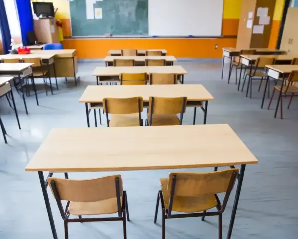 Pusta klasa szkolna z rzędami ławek i krzeseł. W tle tablica i okna. Obowiązek nauki czeka na uczniów.