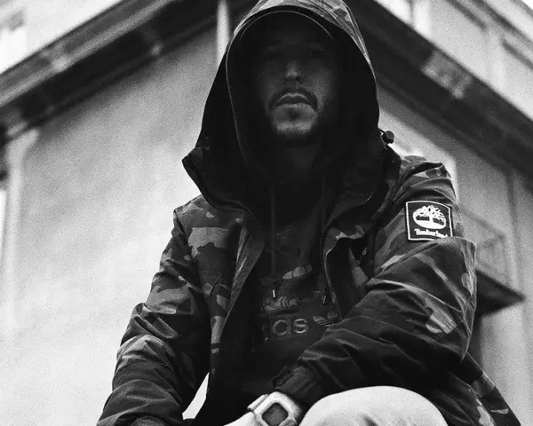 Mężczyzna w kapturze i kurtce moro, z widocznym logo Timberland. Jego styl to ćpaj stajl czlonkowie, gotowy na miejskie wyzwania.