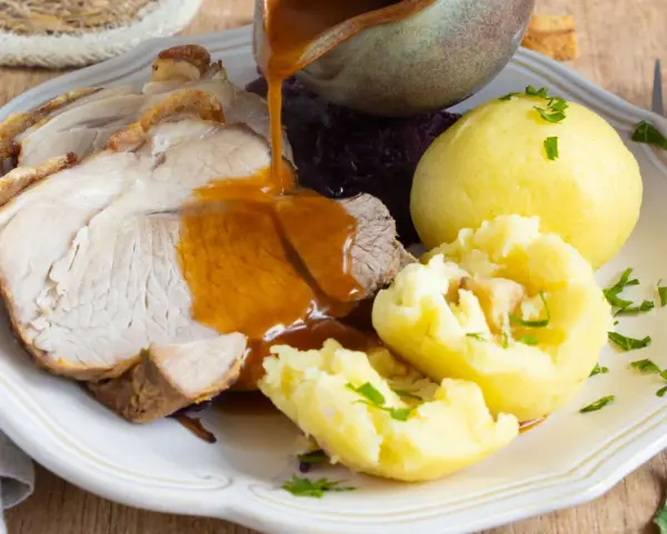 Omas Sonntagsessen: Saftiger Schweinebraten mit knuspriger Kruste, Klößen und Rotkohl, übergossen mit dunkler Soße.