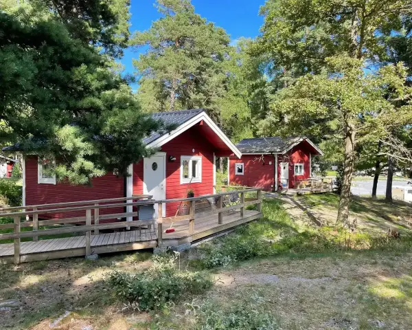 Röda stugor med träaltaner och ramper på Waxholms camping, omgivna av grönska och träd.