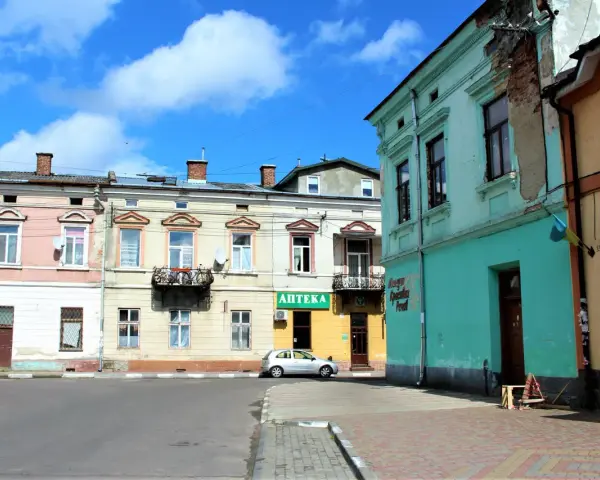 Kolorowe kamienice przy ulicy, gdzie mój stryj kiedyś mieszkał. Srebrny samochód zaparkowany obok apteki.