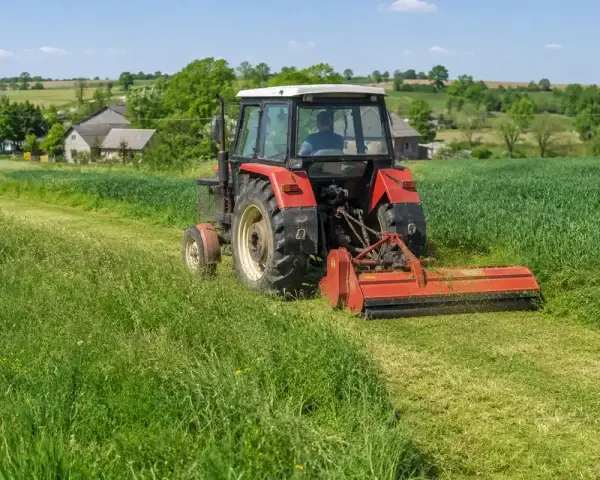 Czerwony traktor z mulczerem do c 330 kosi trawę na zielonym polu. W tle wiejskie domy i drzewa.