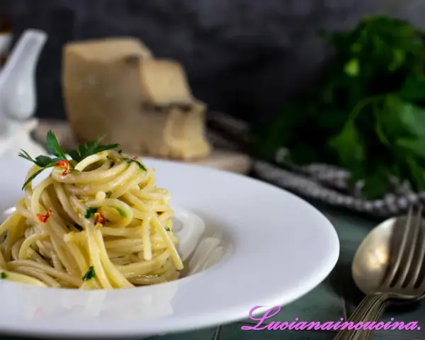 Un piatto di spaghetti alla carrettiera, conditi con aglio, olio, peperoncino e prezzemolo, con pecorino grattugiato sullo sfondo.
