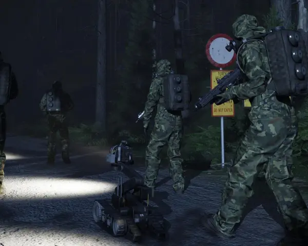 Żołnierze w kamuflażu i robot zwiadowczy na nocnej drodze leśnej.