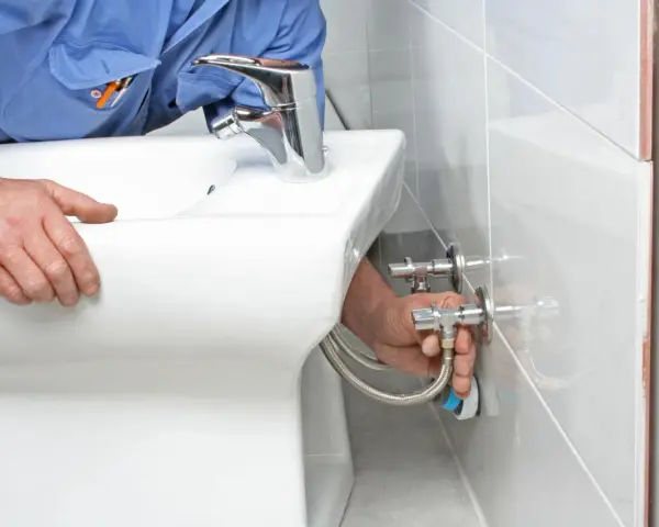 Instalator podłącza wężyki do nowego, białego bidetu.