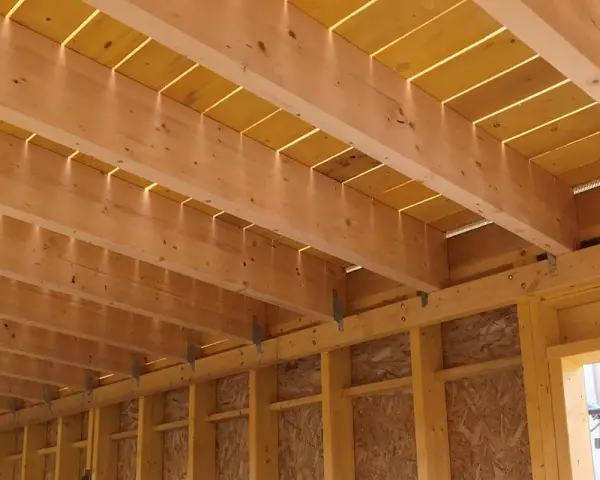 Vue détaillée de comment réaliser le solivage d'un plancher d'étage : poutres en bois, panneaux jaunes et supports métalliques.