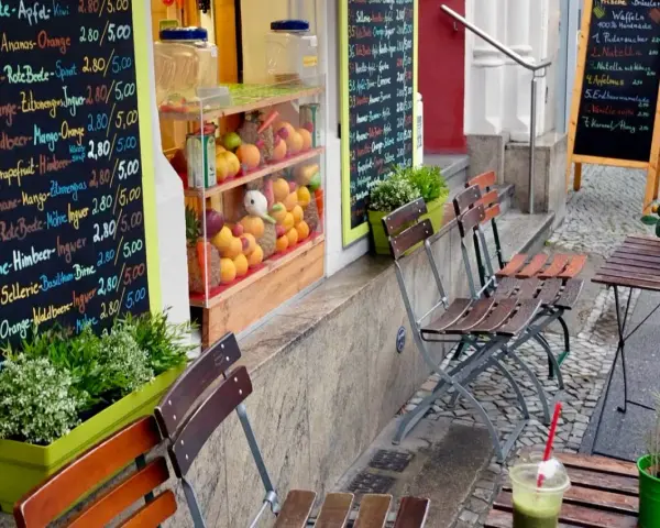 Frischer Smoothie in Berlin. Bunte Tafel mit Frucht- und Gemüsesorten, daneben leere Stühle und ein Tisch.