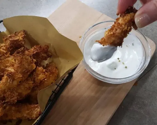 Bocconcini di pollo in friggitrice ad aria, croccanti e dorati, pronti per essere intinti in una salsa cremosa.