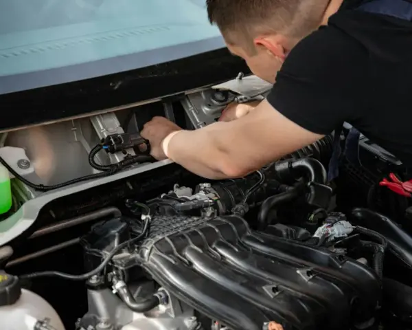 Mechanik naprawia silnik, prawdopodobnie usuwając uciążliwy błąd P0011. Widać zbiornik płynu i elementy silnika.