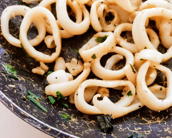 Anelli di totano in padella, dorati e profumati con erbe aromatiche, pronti per essere gustati.