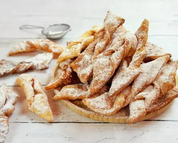 Faworki croccanti e dorati, spolverati di zucchero a velo. Un delizioso dolce da preparare seguendo un semplice faworki przepis.