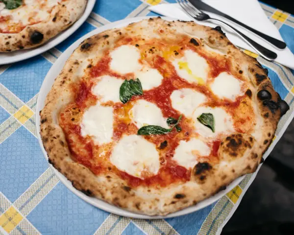 Pyszna pizza napolitana z pomidorami, mozzarellą i bazylią na niebieskim obrusie.