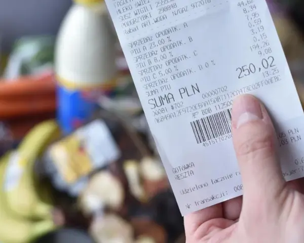 Ręka trzyma paragon z zakupów spożywczych, na którym widnieje suma 250,02 zł. Zastanawiasz się, gdzie wyrzucać paragony? Ten jest z papieru termicznego.