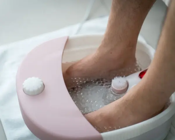 A person's feet are soaking in a foot spa machine filled with bubbly water. You can put water, bath salts, or essential oils in a foot spa machine for a relaxing experience.