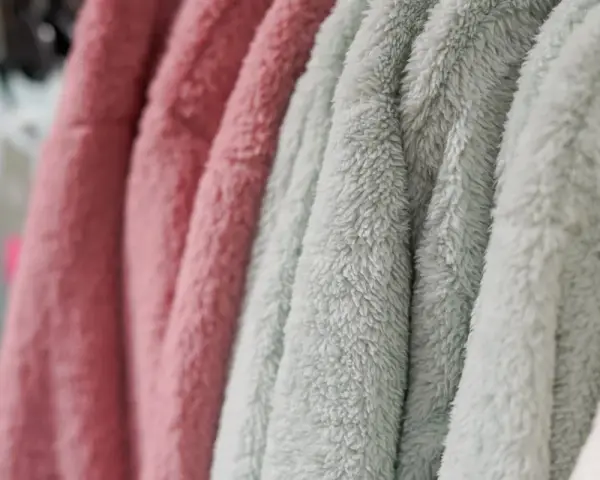 Des vêtements douillets en matière molleton, aux couleurs rose et vert d'eau, sont suspendus sur des cintres.