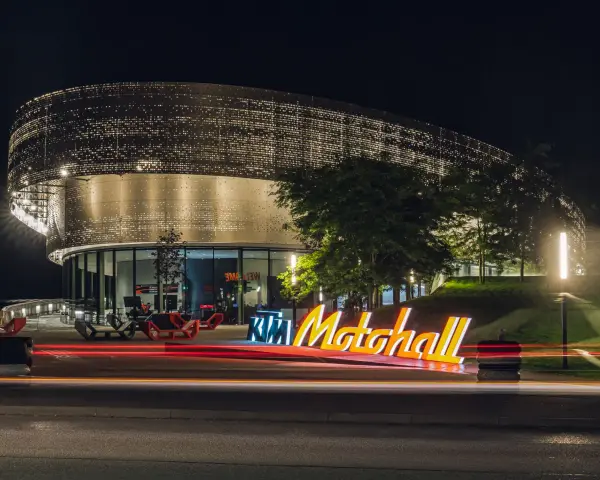 Insegna luminosa KTM Motohall di notte, con il moderno edificio illuminato e le scie luminose delle auto.