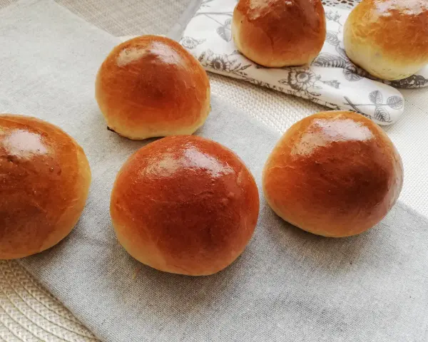 Pięć puszystych bułek maślanych, lśniących od pieczenia, ułożonych na lnianej serwetce. Idealne na śniadanie.
