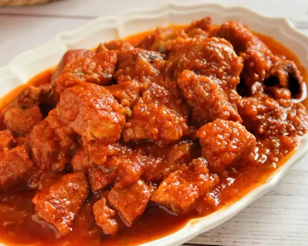 Plato de magro con tomate, trozos de carne tierna en una salsa roja y sabrosa, servido en una fuente blanca.