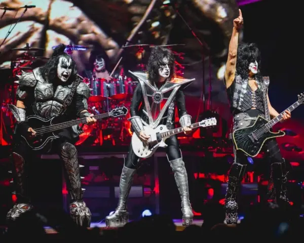 Les membres du groupe de rock Kiss, maquillés et costumés, jouent sur scène. Un chanteur lève un bras en signe de victoire.