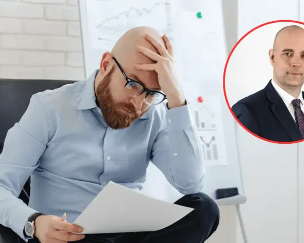 Zmartwiony mężczyzna analizuje dokumenty, podczas gdy w tle widać portret biznesmena. Obraz symbolizuje analizę przyczyn bezrobocia w Polsce.