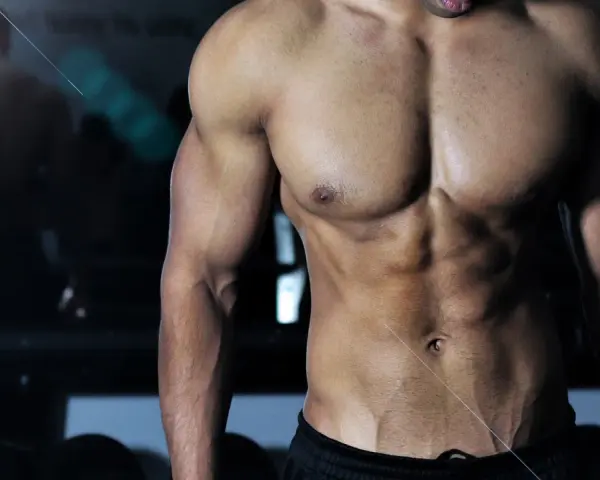 Muskulös man med synliga magmuskler i gym. En spegelbild av en annan person syns i bakgrunden. Frågan "hur deffar man" kan besvaras med denna fysik.