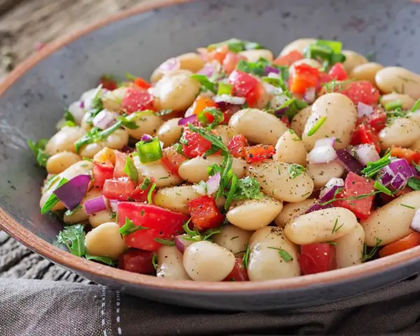 Un'insalata di fagioli sfiziosa, ricca di pomodori freschi, cipolla rossa e erbe aromatiche, servita in una ciotola rustica.