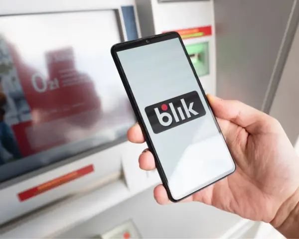 Dłoń trzyma smartfon z logo Blik. Czy Blik jest tylko w Polsce? Płatność zbliżeniowa przy bankomacie.