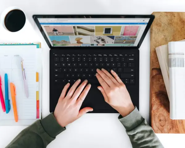 Hände tippen auf einem Laptop, daneben ein Kalender und eine Kaffeetasse.