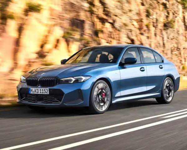 Niebieskie BMW klasy średniej jedzie po krętej drodze w skalistym krajobrazie.