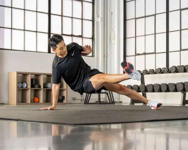 Un homme en tenue de sport exécute un exercice de planche latérale dans une salle de sport.