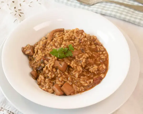 Arroz con sepia en un plato blanco, decorado con perejil.