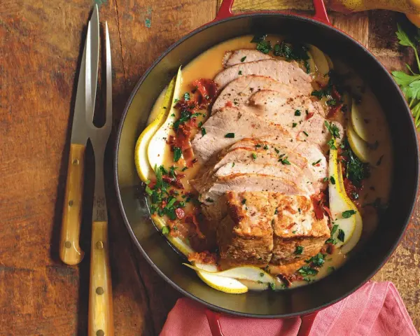 Lonza di maiale in padella morbida, affettata e servita con pere, salsa cremosa e prezzemolo tritato.