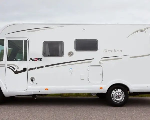 Vit husbil, Pilote G740 Aventura, parkerad vid en väg med gräs och träd i bakgrunden.