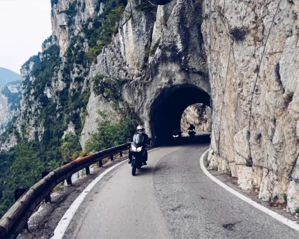 Motocykliści przemierzają malowniczą strada della forra, wjeżdżając w skalny tunel. Widok na jezioro i góry zapiera dech.